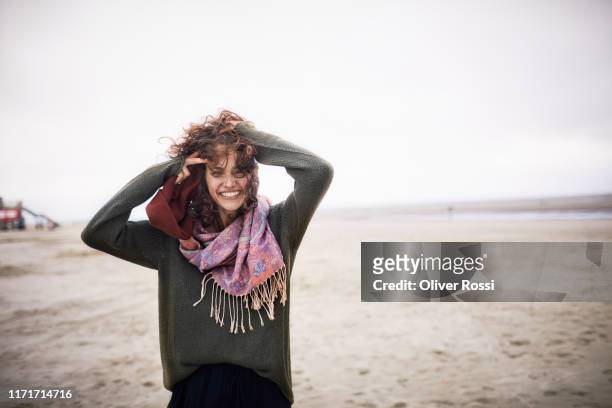 portrait of happy woman with windswept hair on the beach - overcast beach stock pictures, royalty-free photos & images
