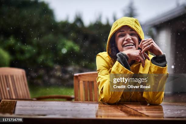 portrait of happy woman wearing raincoat during heavy rain in garden - arbeitskleidung stock-fotos und bilder