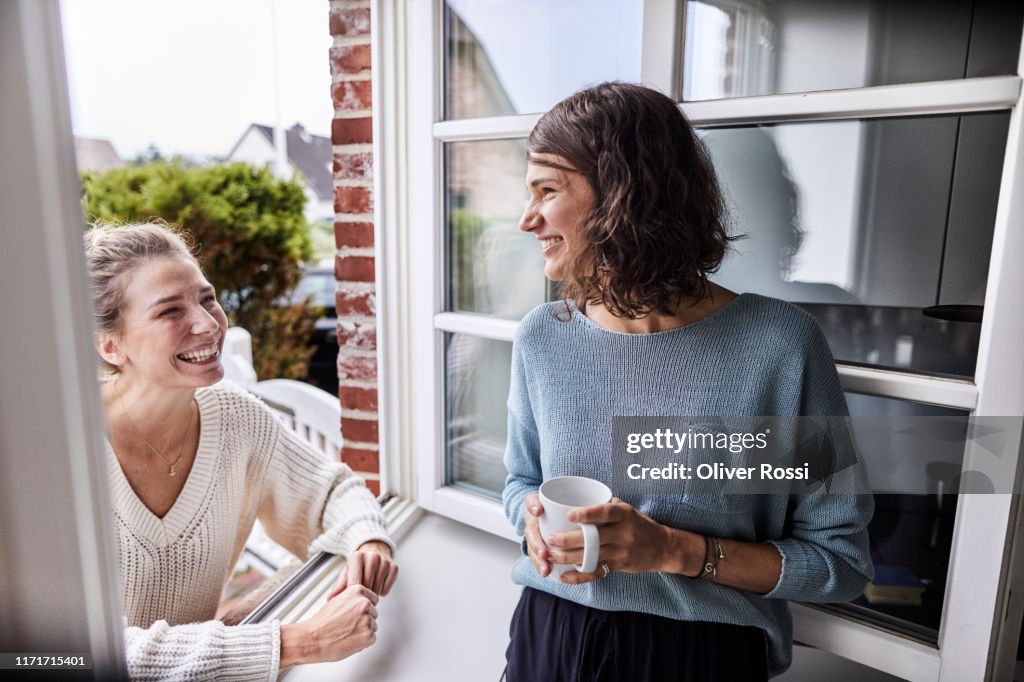 Two happy women talking through the window