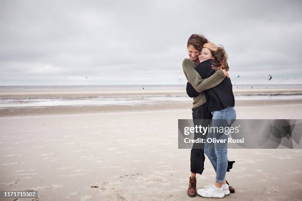 happy young woman hugging girl on the beach - zus stockfoto's en -beelden