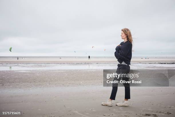 pensive woman standing on the beach - casual woman pensive side view stockfoto's en -beelden