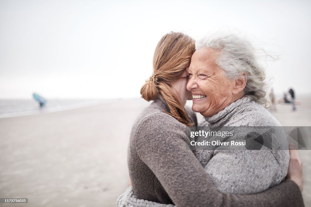 Affectionate grandmother and granddaughter hugging on the beach