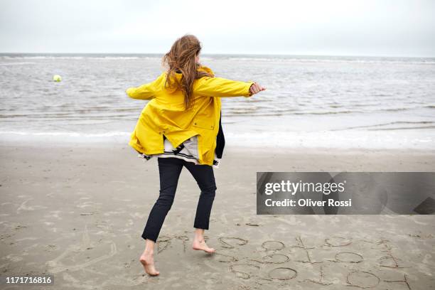 carefree woman wearing raincoat running on the beach - leuchtende farbe stock-fotos und bilder