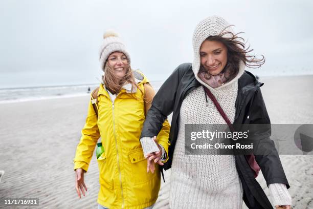 two happy women in warm clothing on the beach - raincoat stock-fotos und bilder