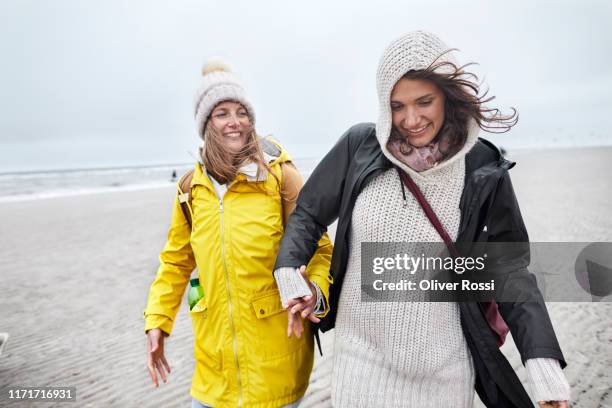 two happy women in warm clothing on the beach - raincoat stockfoto's en -beelden