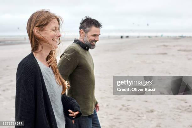 happy couple walking hand in hand on the beach - adulto de mediana edad fotografías e imágenes de stock