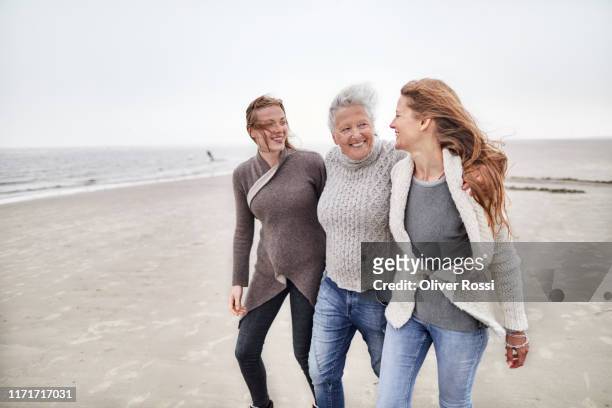 grandmother, mother and daughter walking on the beach - nur frauen stock-fotos und bilder