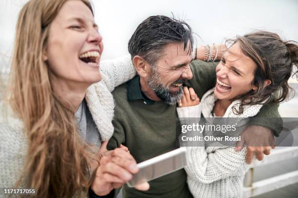laughing man and two women with smartphone by the sea - männer gruppe stock-fotos und bilder