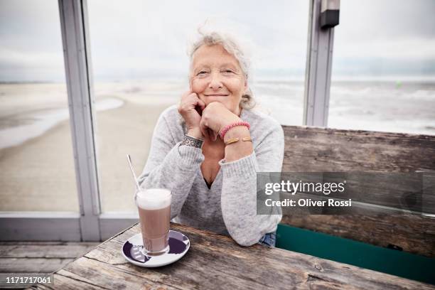 portrait of smiling senior woman in a cafe by the sea - bench sea stock-fotos und bilder