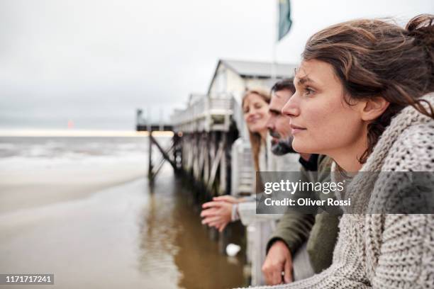 man and two women leaning on railing by the sea - contemplation family stock-fotos und bilder