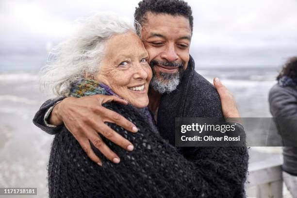 portrait of senior woman and mature man hugging by the sea - tossing hair facing camera woman outdoors stock pictures, royalty-free photos & images