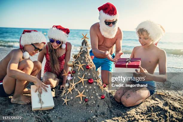 family opening gift under sand christmas tree. - summer christmas stock pictures, royalty-free photos & images