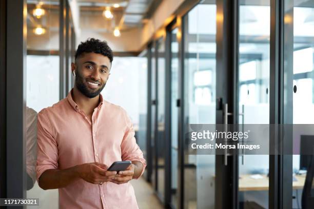 smiling young businessman holding mobile phone - geschäftsmann im büro mobiltelefon stock-fotos und bilder