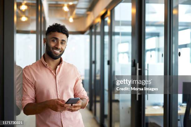 smiling young businessman holding mobile phone - indian subcontinent ethnicity stock pictures, royalty-free photos & images