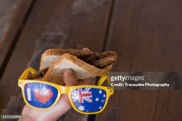 male teenager holding a sausage on bread and a pair of australian flag sunglasses. - australia day flag stock pictures, royalty-free photos & images