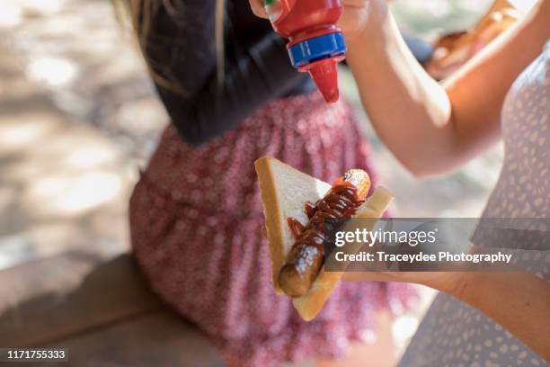 a female teenager preparing a sausage on bread at a barbecue. - summer sausage stock pictures, royalty-free photos & images