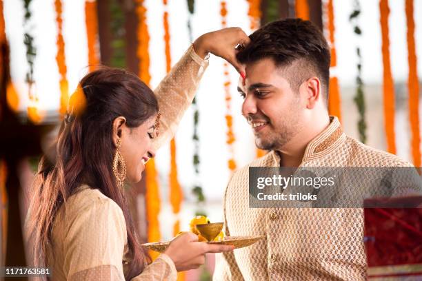 sister applying tilaka to brother on raksha bandhan - raksha bandhan stock pictures, royalty-free photos & images