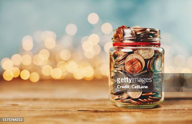 tarro de dinero de donación lleno de monedas frente a las luces navideñas - dar fotografías e imágenes de stock