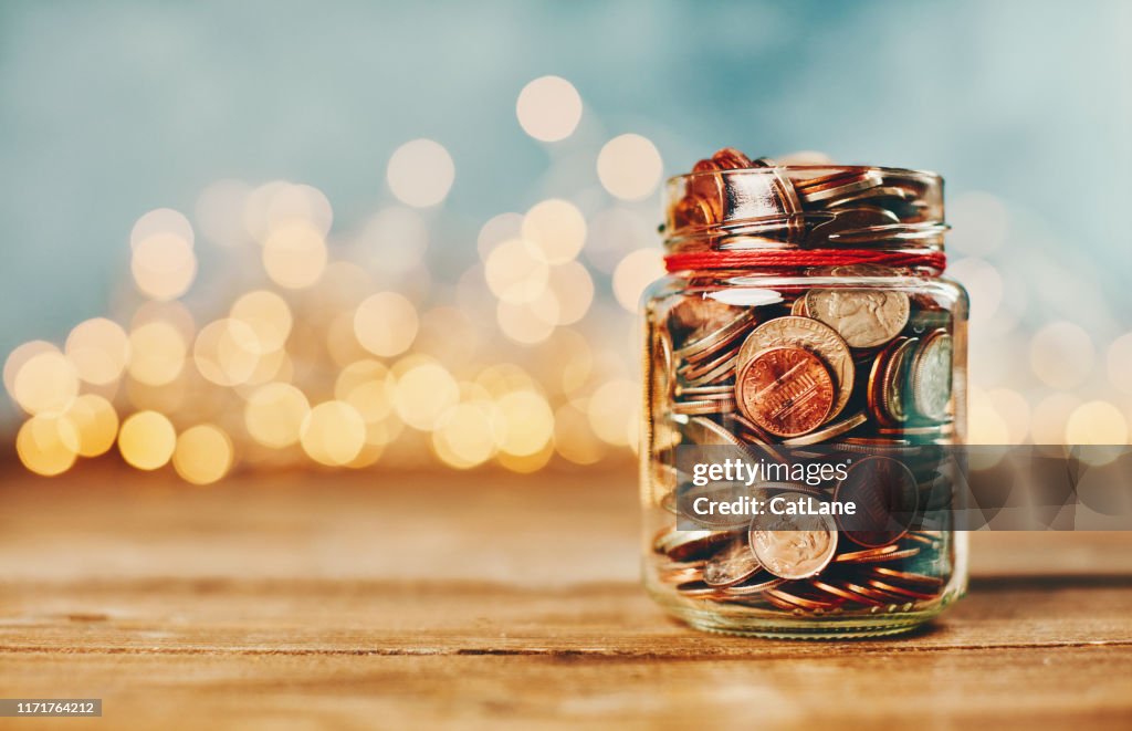 Donation money jar filled with coins in front of holiday lights