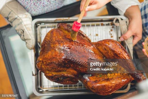 preparing stuffed turkey for thanksgiving dinner, daughter helping mother to baste turkey - basted stock pictures, royalty-free photos & images