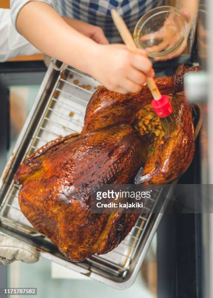 preparing stuffed turkey for thanksgiving dinner, daughter helping mother to baste turkey - basted stock pictures, royalty-free photos & images