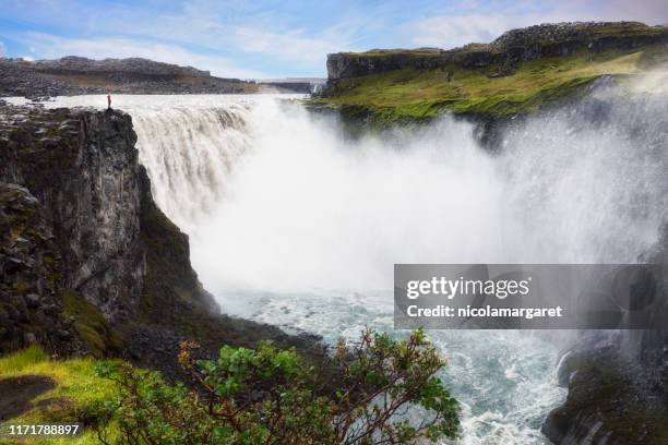dettifoss, islanda con una piccola figura in piedi sulla scogliera - dettifoss waterfall foto e immagini stock
