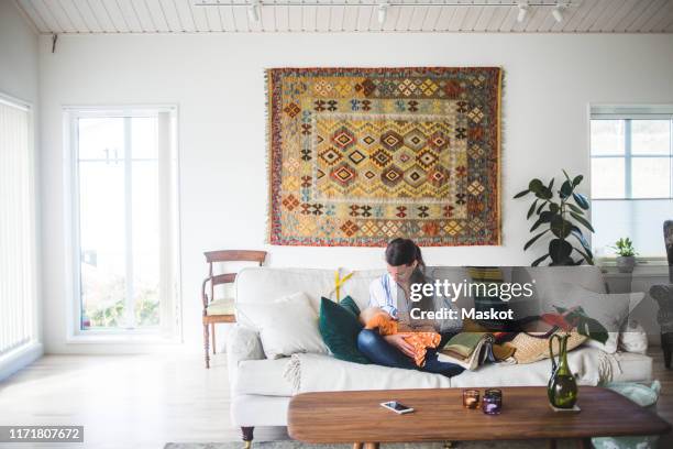 multi-tasking design professional breastfeeding daughter while sitting on sofa in living room at home - panô - fotografias e filmes do acervo