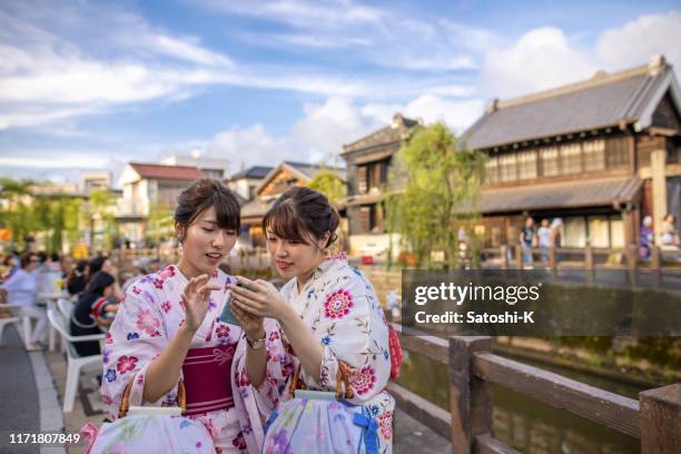 young sisters in yukata using smart phone at traditional japanese festival - yukata stock pictures, royalty-free photos & images