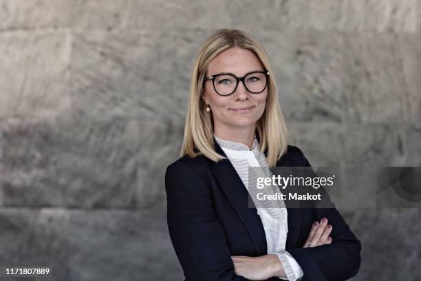 portrait of businesswoman with arms crossed standing against wall in office - donne 35 anni foto e immagini stock