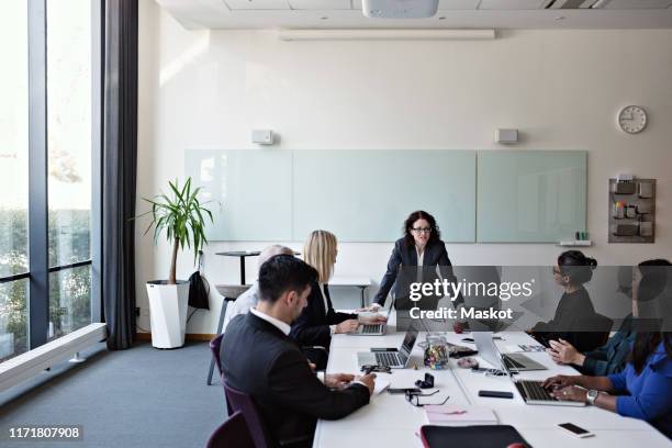 businesswoman interacting with colleagues sitting at conference table during meeting in board room - chief executive officer stock pictures, royalty-free photos & images