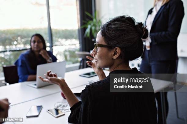 businesswoman gesturing while discussing with colleagues during meeting at conference table in board room - chief executive officer stock-fotos und bilder