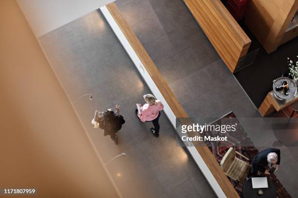 high angle view of female colleagues discussing while walking in corridor at office - floor walk business stock pictures, royalty-free photos & images