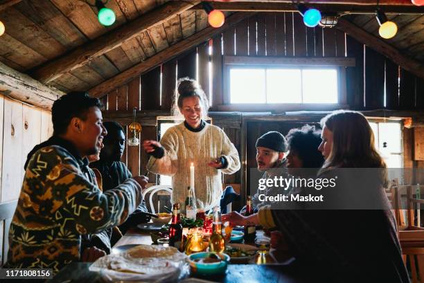 smiling young woman talking while enjoying meal with friends in cottage - log cabin stock pictures, royalty-free photos & images