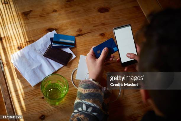 high angle view of young man doing online shopping over credit card on wooden table at home - rural banking stock-fotos und bilder