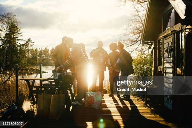 silhouette friends talking while standing outside cottage in front of lake during sunset - cabin scandinavia stock pictures, royalty-free photos & images
