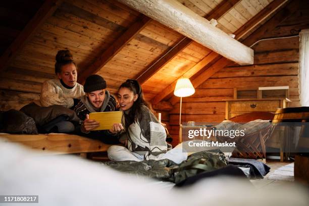 male and female friends watching movie over digital tablet while relaxing in cottage - filmabend stock-fotos und bilder