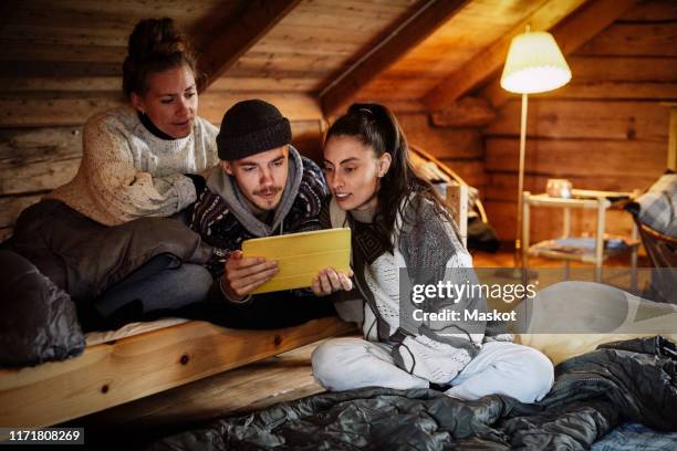 friends watching movie over digital tablet while relaxing in cottage - combles photos et images de collection