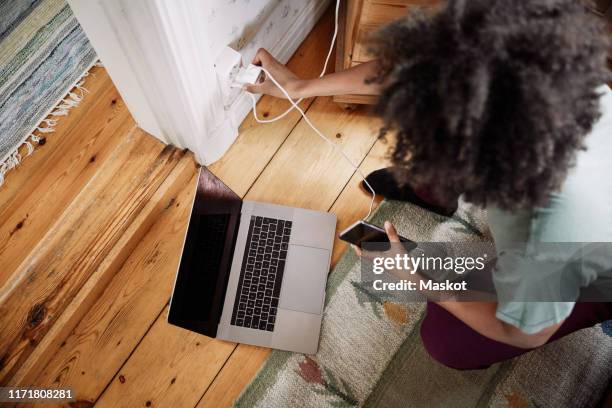 high angle view of young woman plugging mobile phone charger in electrical outlet at home - stecker stock-fotos und bilder