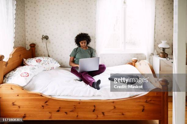 high angle view of young woman using laptop while relaxing on bed at home seen through doorway - pillow icon stock pictures, royalty-free photos & images