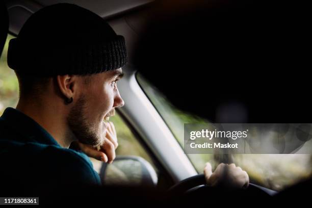 smiling young man wearing knit hat while driving car - car scandinavia stock pictures, royalty-free photos & images