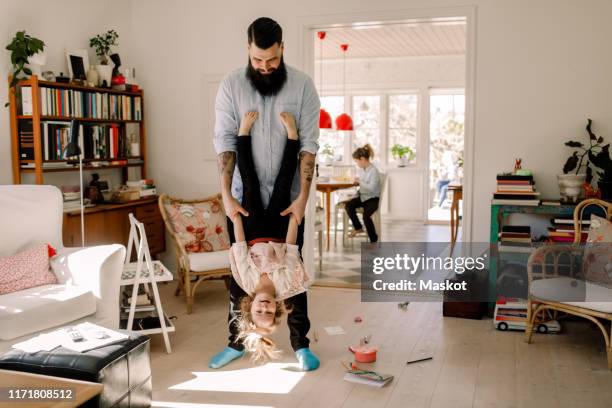 playful father swinging girl while standing in living room at home - living room kids stockfoto's en -beelden