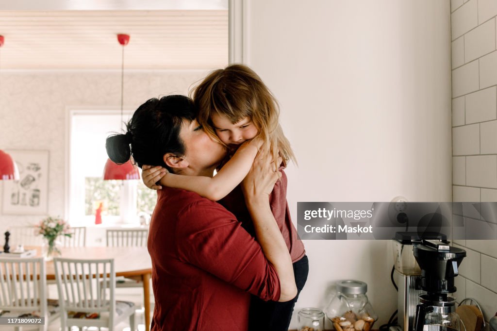 Side view of mother kissing sad daughter at home