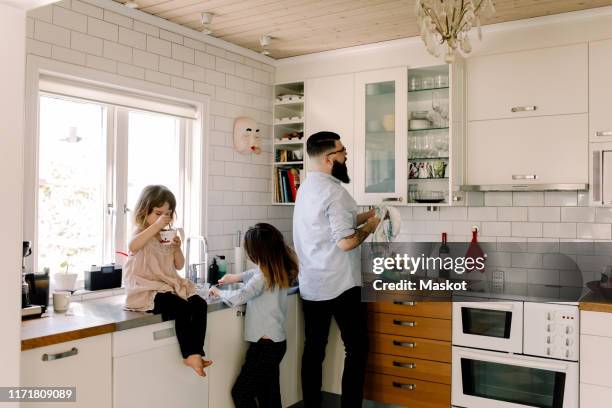 father and daughter working at counter while girl eating food in kitchen - hipster in a kitchen stock-fotos und bilder