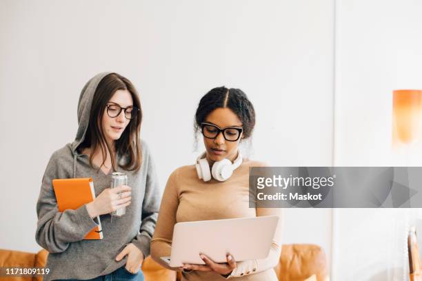 female computer programmers discussing over laptop while standing in office - we can do it stock pictures, royalty-free photos & images