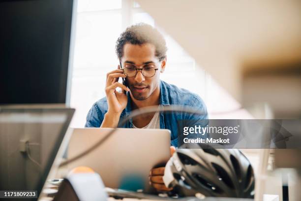 computer programmer talking on smart phone while using laptop in creative office - answering stock pictures, royalty-free photos & images