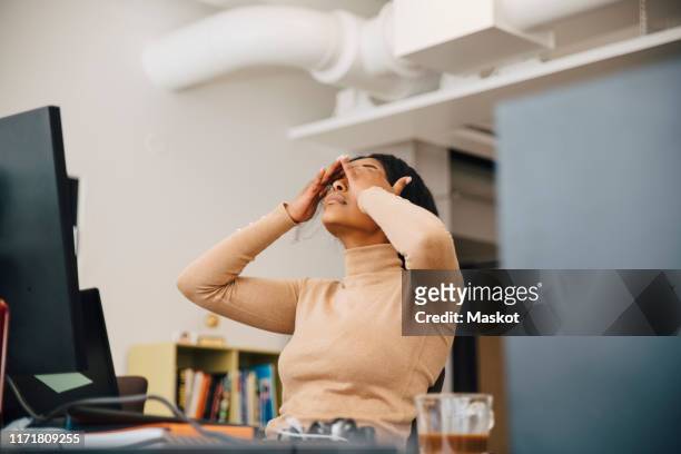 frustrated female computer programmer with head in hands sitting in creative office - werken stockfoto's en -beelden