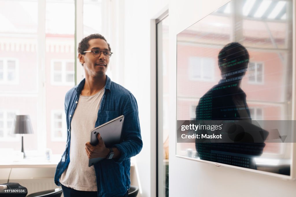 Computer hacker looking at code on television screen while standing in creative office