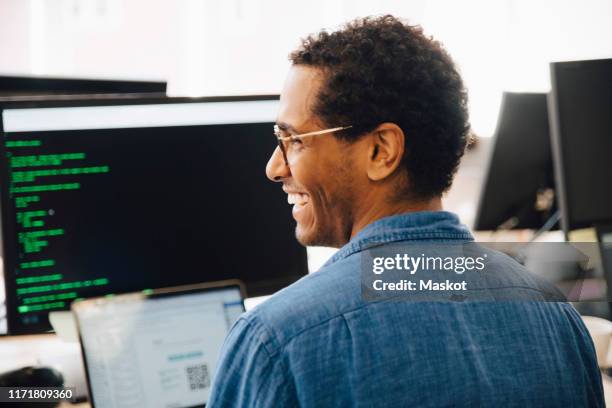 rear view of cheerful male it professional looking away while sitting in creative office - developers coding stock pictures, royalty-free photos & images