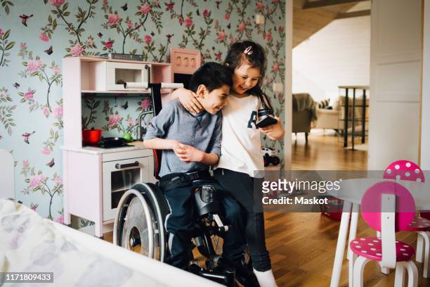 cheerful sister watching video with autistic brother on mobile phone at home - special needs children stock pictures, royalty-free photos & images