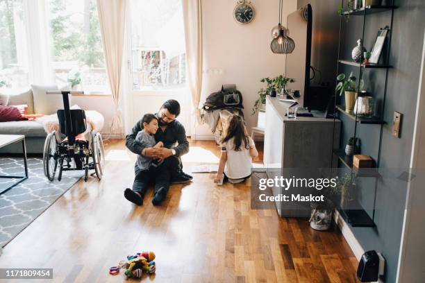 high angle view of father holding autistic son while sitting by daughter on floor at home - mental disability stock pictures, royalty-free photos & images